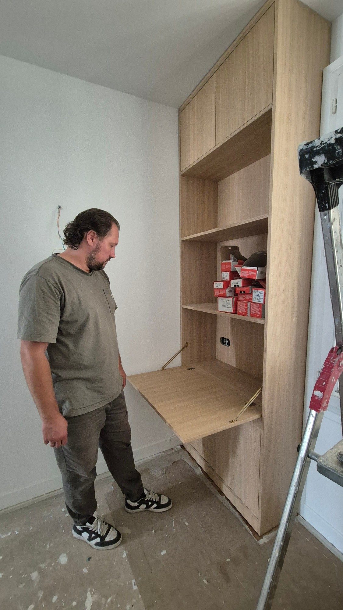 Compagnon examinant une menuiserie sur mesure en cours de pose, avec tablette rabattable et rangements en bois clair.